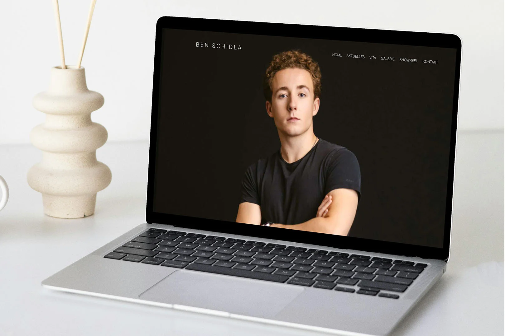 webseite Referenz auf MacBook zu sehen, dahinter Vase auf weißem Tisch